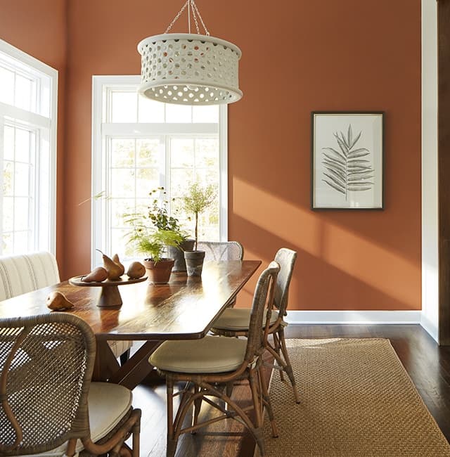 Sunlit dining room with a warm terracotta painted wall, cream seating and a natural wood table